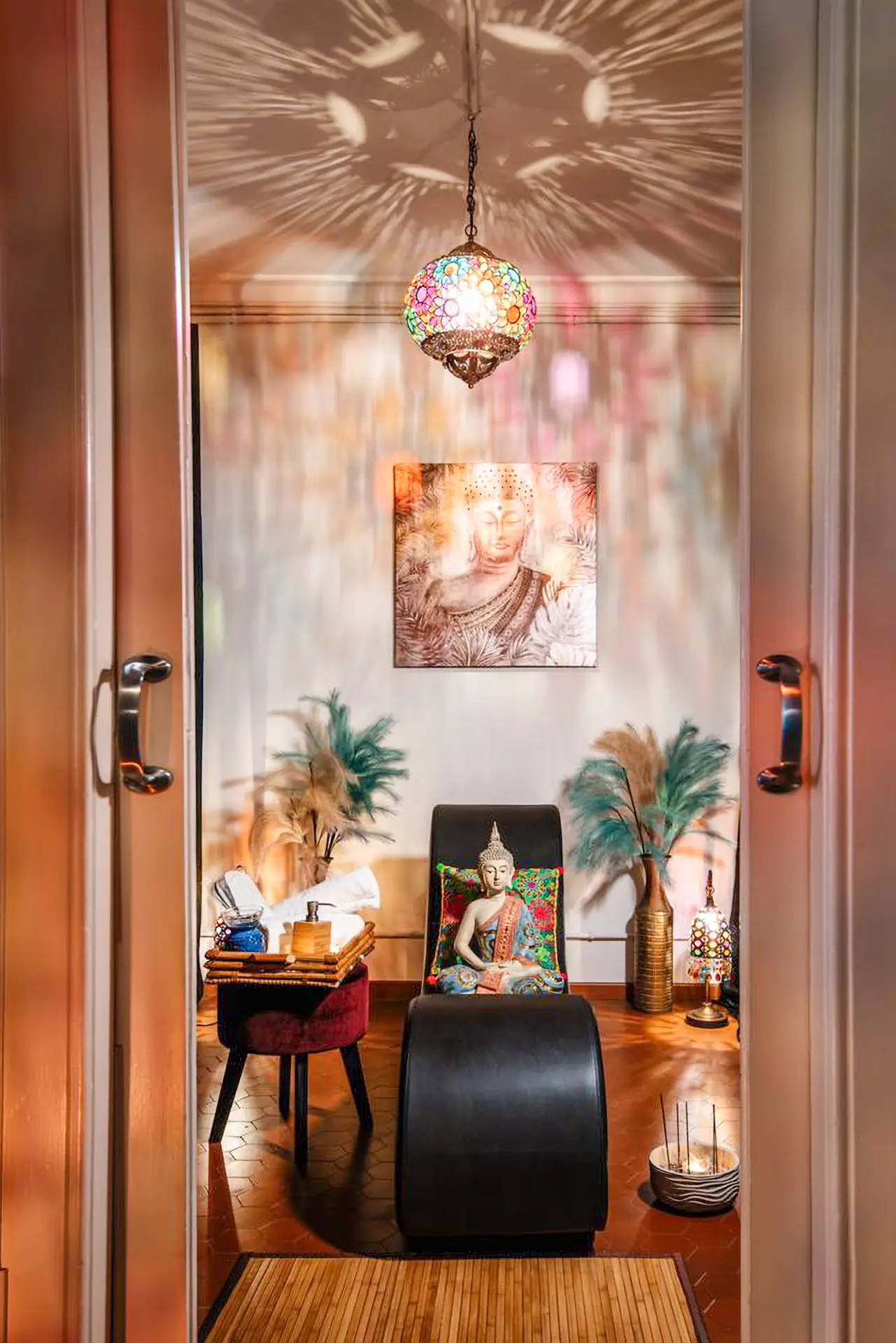 Cabina de Siam Erotic Massage con diván de masaje, lámpara marroquí de colores y cuadro de Buda